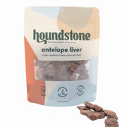 A stand-up pouch of Houndstone Antelope Liver freeze dried dog treats with several dog treats placed in front on a white background.