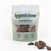 A 2 oz bag of Houndstone Red Tail Deer freeze-dried cat treats, shown on a clean white background with several cat treats scattered in front of the bag.